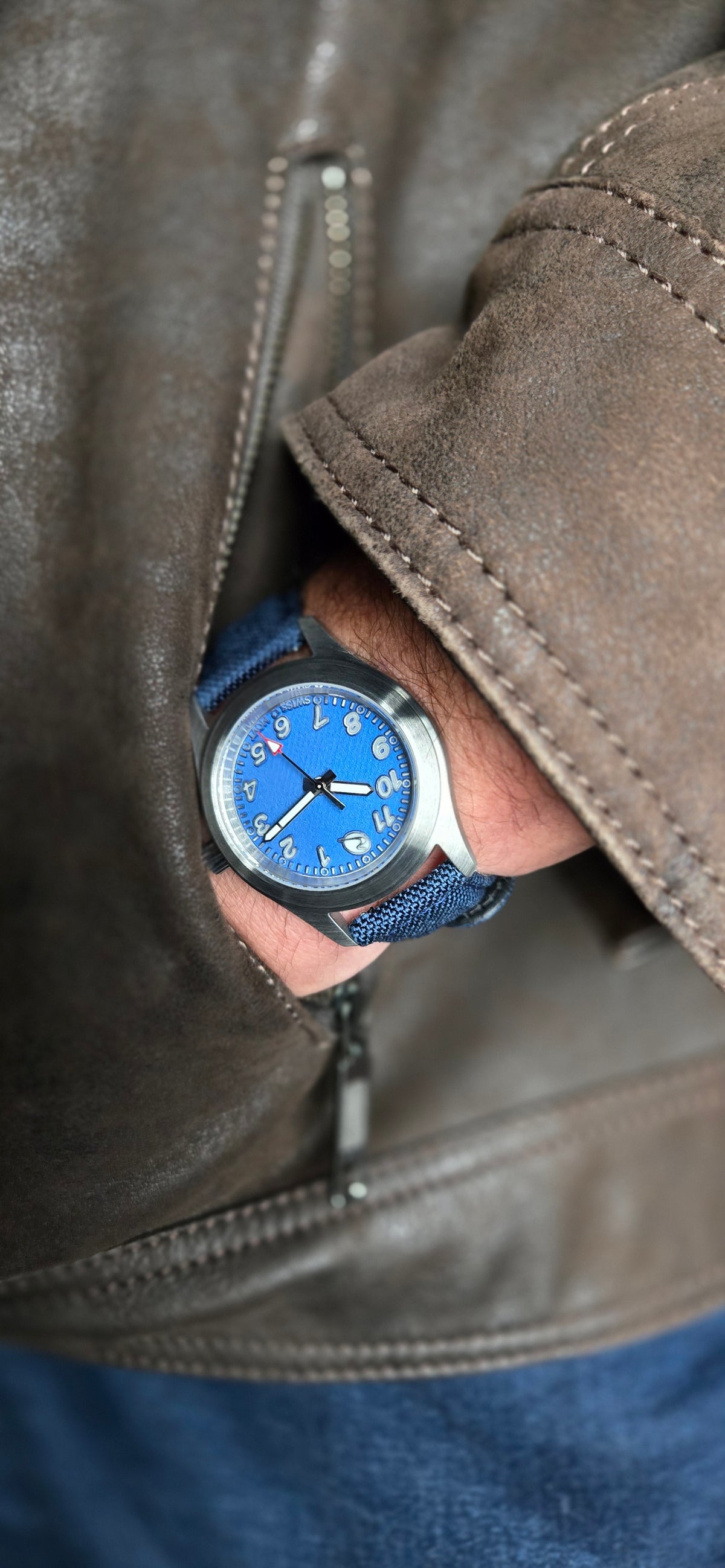 Beck Watch Co. Bearing Cobalt A close-up of a wrist wearing a blue dial watch with a blue strap, tucked under the cuff of a brown leather jacket.